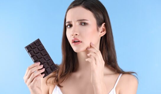 O femeie frumoasă care ține în mână ciocolată, fiind unul dintre acele alimente care cauzează apariția acneei