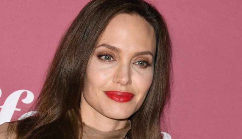 Angelina Jolie cu un machiaj natural și ruj roșu în timp ce pozează la un eveniment dedicat femeilor
