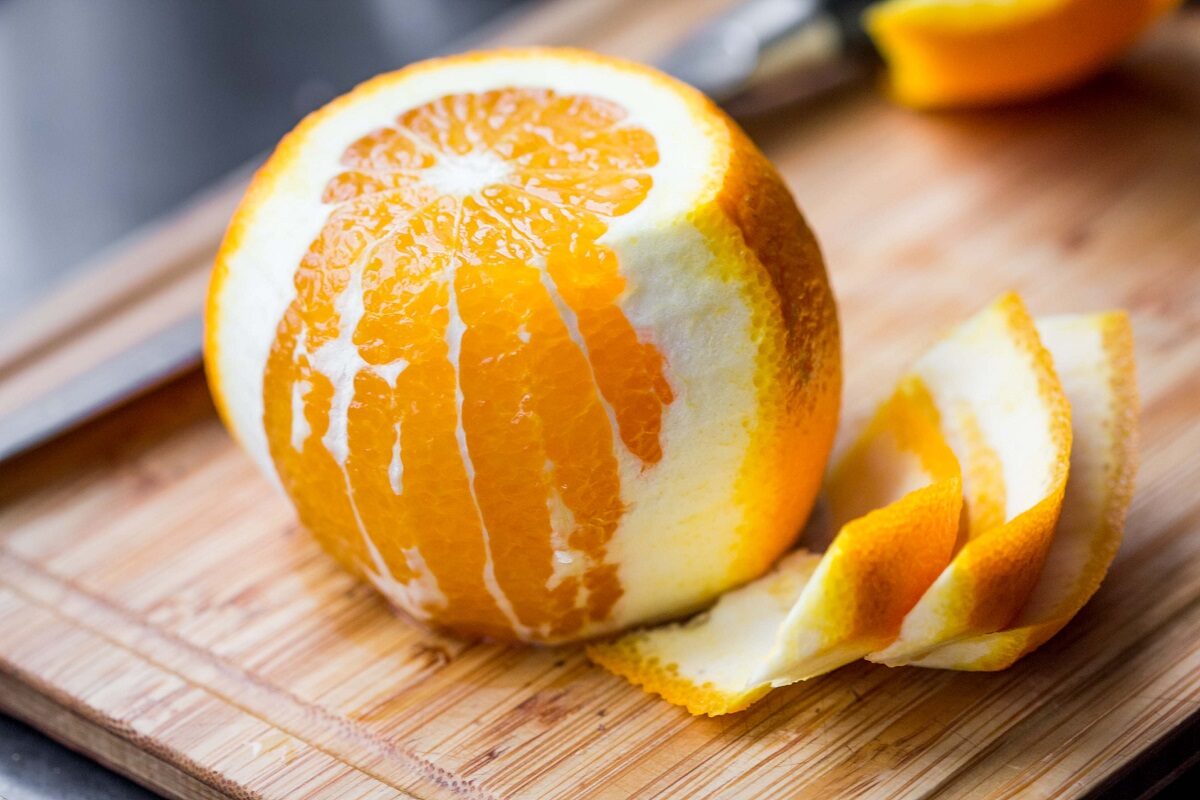 O portocală pe jumătate decojită pe un tocător de lemn în timp ce sugerează beneficiile cojilor de portocale