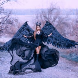 O femeie frumoasă care poartă o rochie neagră și aripi cu pene negre în timp ce înfățișează una din cele mai toxice zodii