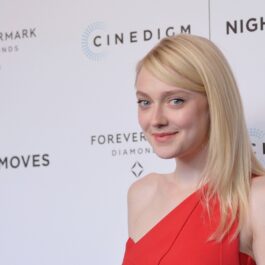 Dakota Fanning într-o rochie roșie pe umăr în timp ce pozează pe covorul roșu la premiera filmului Night Moves