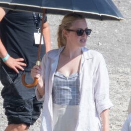 Dakota Fanning în timp ce se ascunde de soare sub o umbrelă pe o plajă din Italia