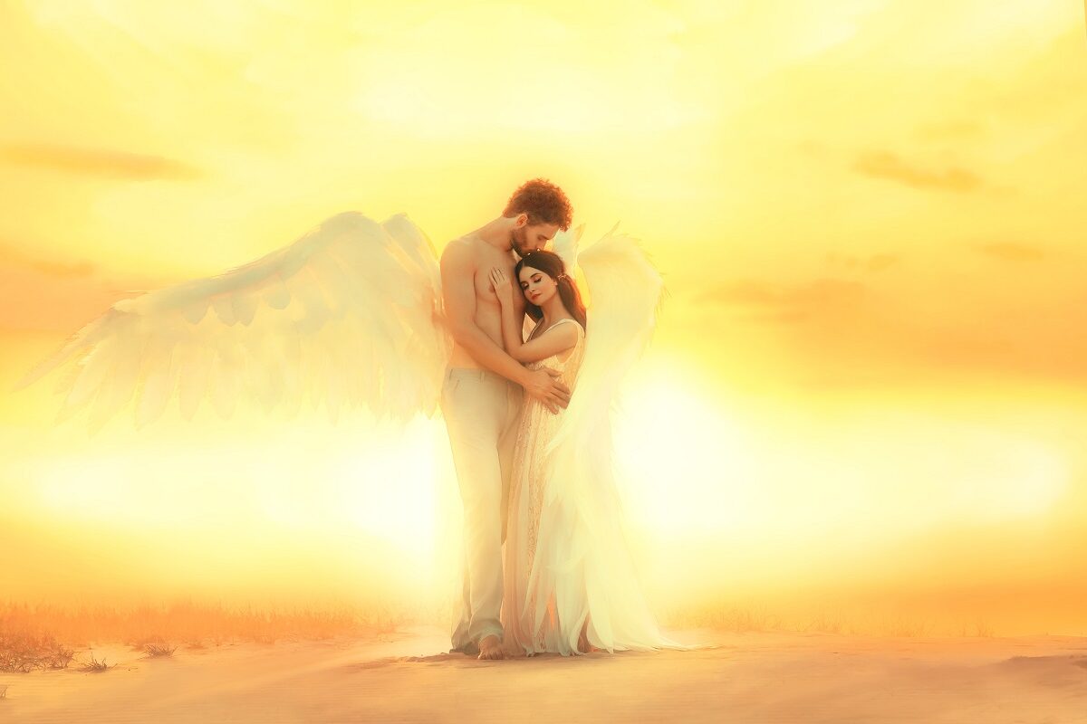 Un cuplu de îndrăgostiți în timp ce se țin în brațe într-un peisaj în care apune soarele