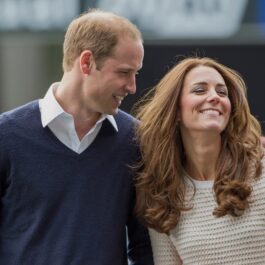 Prințul William într-un hanorac albastru în timp ce o ține după umeri pe Kate Middleton într-un pulover alb