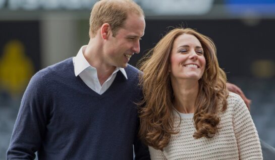 Prințul William într-un hanorac albastru în timp ce o ține după umeri pe Kate Middleton într-un pulover alb