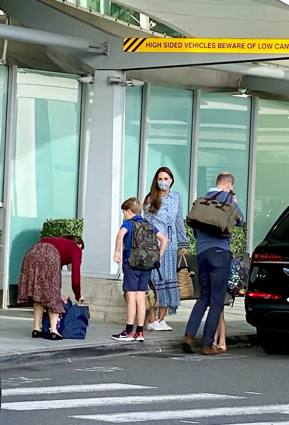 Prințul William cărând un bagaj în spate alturi de Kate Middleton și copiii lor în aeroortul din Londra