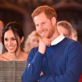 Meghan Markle într-un costum gri alături de Prințul Harry într-un pulover albastru la o ceremonie oficială din Marea Britanie