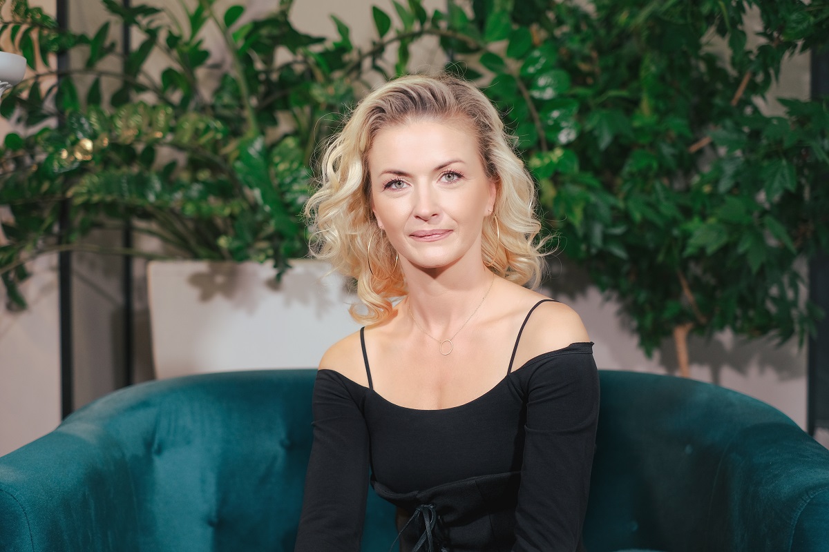 Elwira Petre într-o rochie neagră în timp ce stă pe o canapea albastră pentru interviul Catine.ro