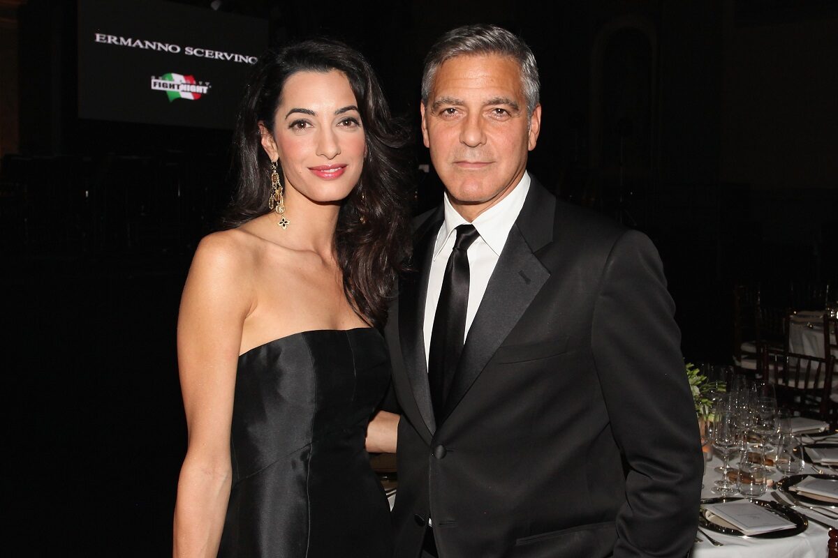 George și Amal Clooney, 2014, la Celebrity Fight Night. Amândoi sunt îmbrăcați în negru. George poartă un costum negru, cu o cămașă albă și o cravată neagră. Amal poartă o rochie neagră fără bretele