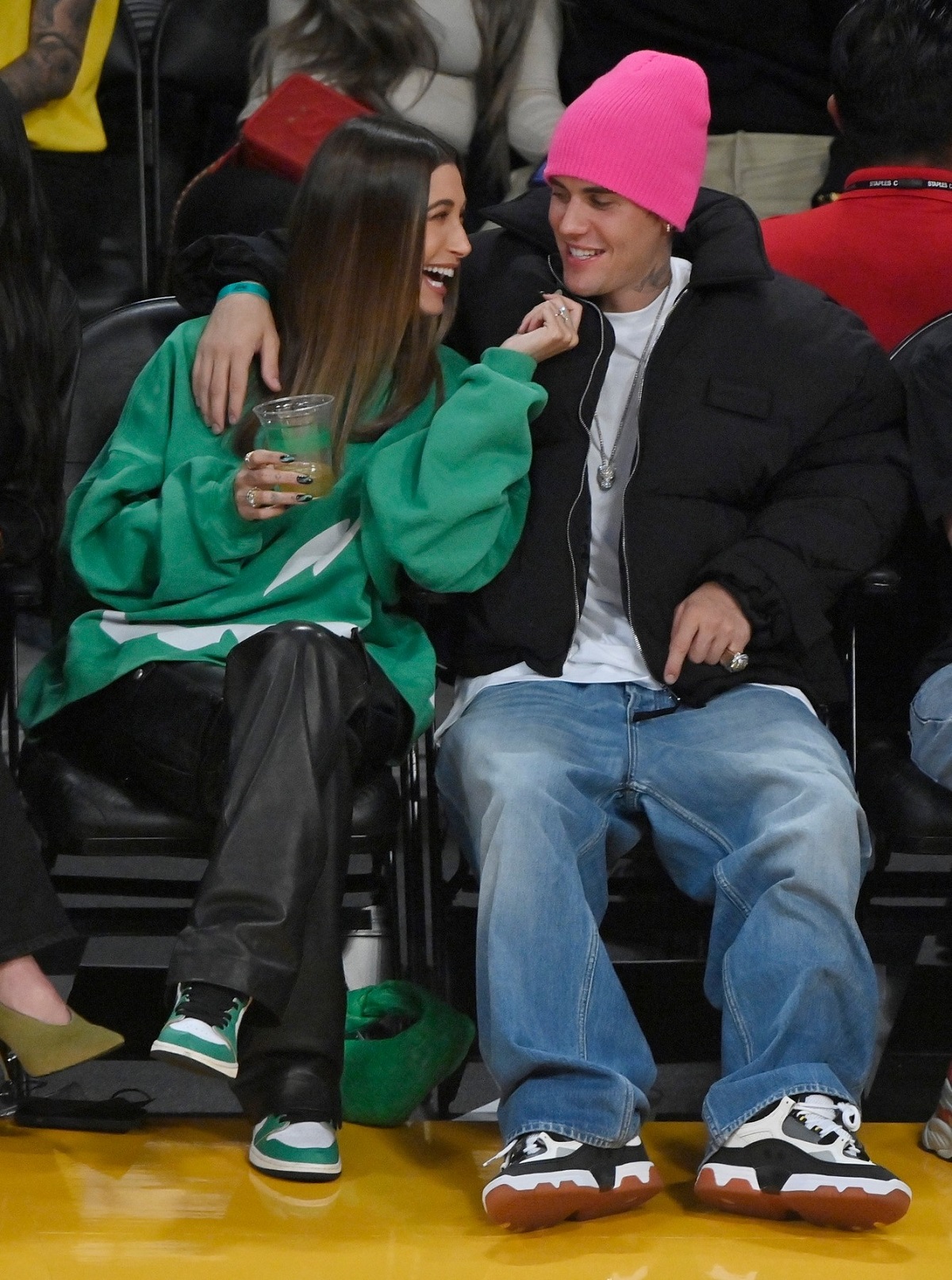 Hailey Bieber într-un hanorac verde în timp ce râde și stă lângă Justin Bieber