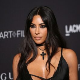 Kim Kardashian într-o rochie neagră cu un lănțisor negru la gât în timp ce pozează pe covorul roșu