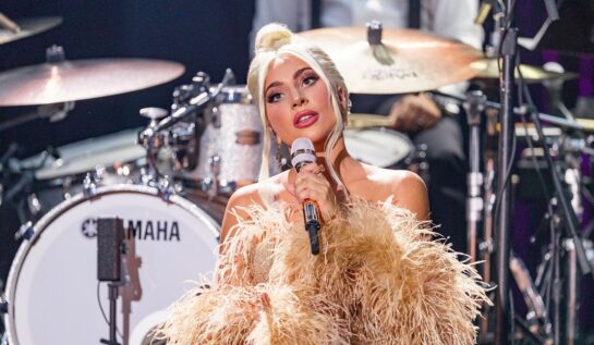 Lady Gaga într-o rochie aurie cu blană în timp ce se află pe scenă și cântă, după ce a s-a fotografiat fără machiaj