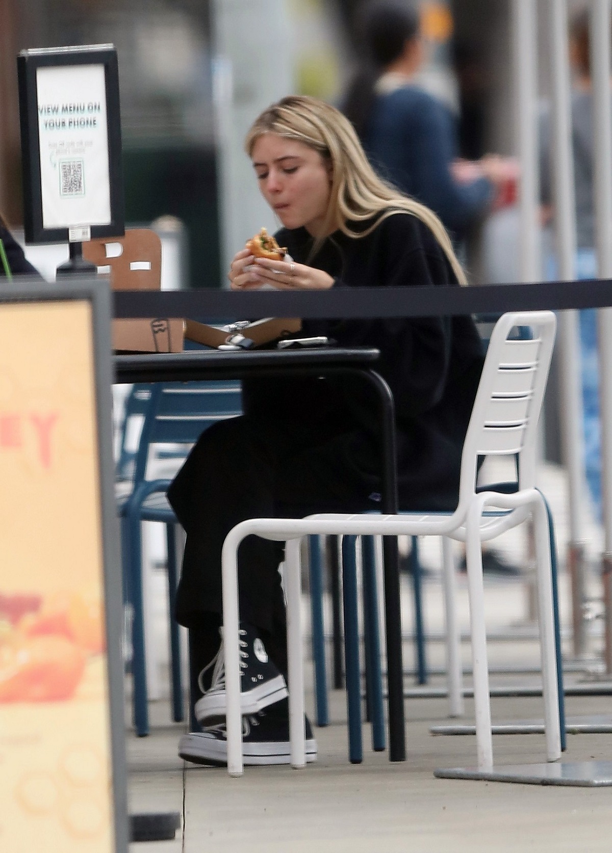 Leni Klum într-un trening negru în timp ce stă la o masă și mănâncă un burger
