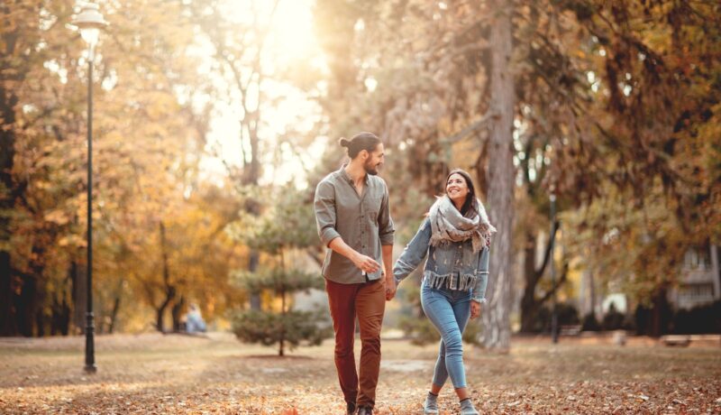 Un cuplu de îndrăgostiți care se țin de mână și se plimbă într-un parc din București toamna