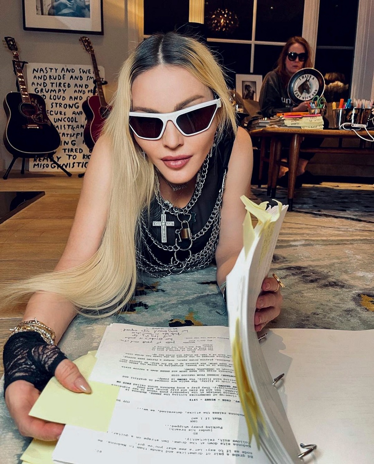 Madonna întinsă pe un covor în timp ce citește un contract și poartă ochelari de soare negri