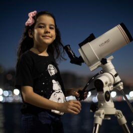 Nicole Oliveira e cea mai tânără astronomă din lume, la doar 8 ani. Ea colaborează cu un proiect NASA. În imagine poartă un tricou negru, o fundă roz, și se uită printr-un telescop alb