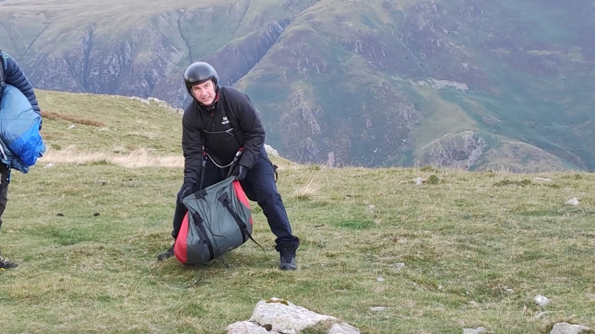 Tom Cruise alături de echipa de filmare pe un munte în timp ce își pregătește parașuta