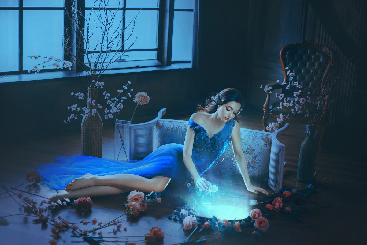 O femeie frumoasă care stă întinsă pe podea într-o rochie albastră în timp ce privește în oglindă
