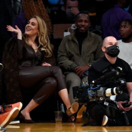 Adele salută pe cineva în timp ce se află în tribune la un meci de baschet, îmbrăcată într-un costum din piele