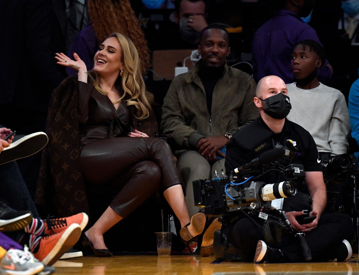 Adele salută pe cineva în timp ce se află în tribune la un meci de baschet, îmbrăcată într-un costum din piele