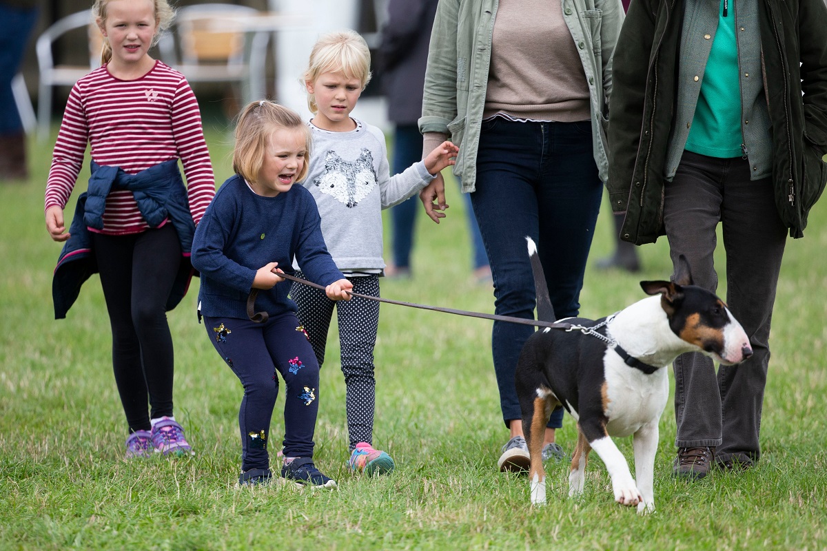 Isla și Savannah Phillips alături de terrierul Prințesei Anne, în 2018. Îl țin de lesă, fundalul e cu verde, iarbă
