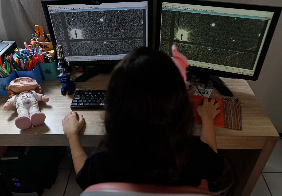 Nicole Oliveira, cea mai tânără astronomă din lume, studiază imagini cu cerul pe două monitoare de calculator. E îmbrăcată în negru și are o fundă roz în cap