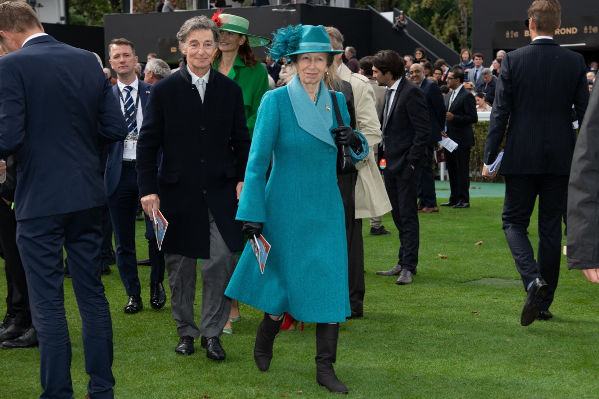 Prințesa Anne, la Prix Qatar Arc de Triomphe, în 2021, Paris. A purtat o haină turcoaz, cu o pălărie în ton. Pe fundal e verdeață, cu bărbați îmbrăcați în negru