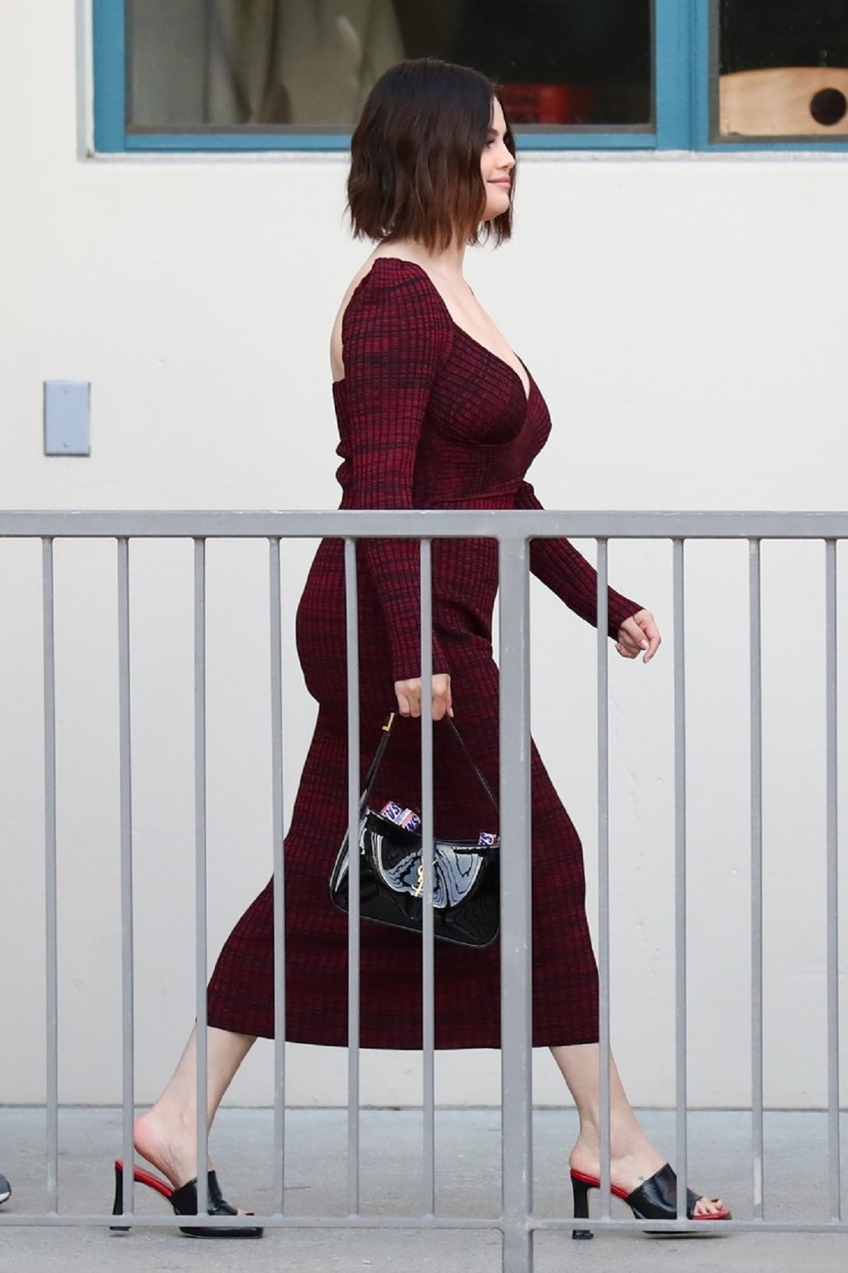 Selena Gomez într-o rochie burgundy în tip ce se află după un gard de protecție