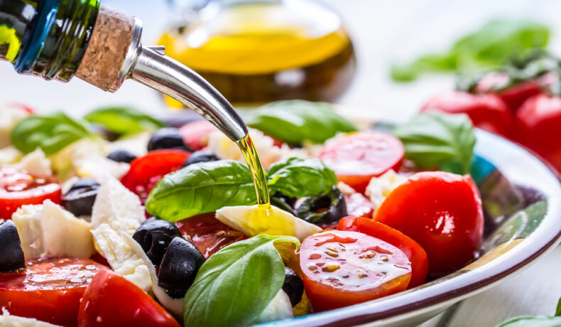 Un bol de salată cu alimente permise în dieta mediteraneană în care se toarnă ulei de măsline