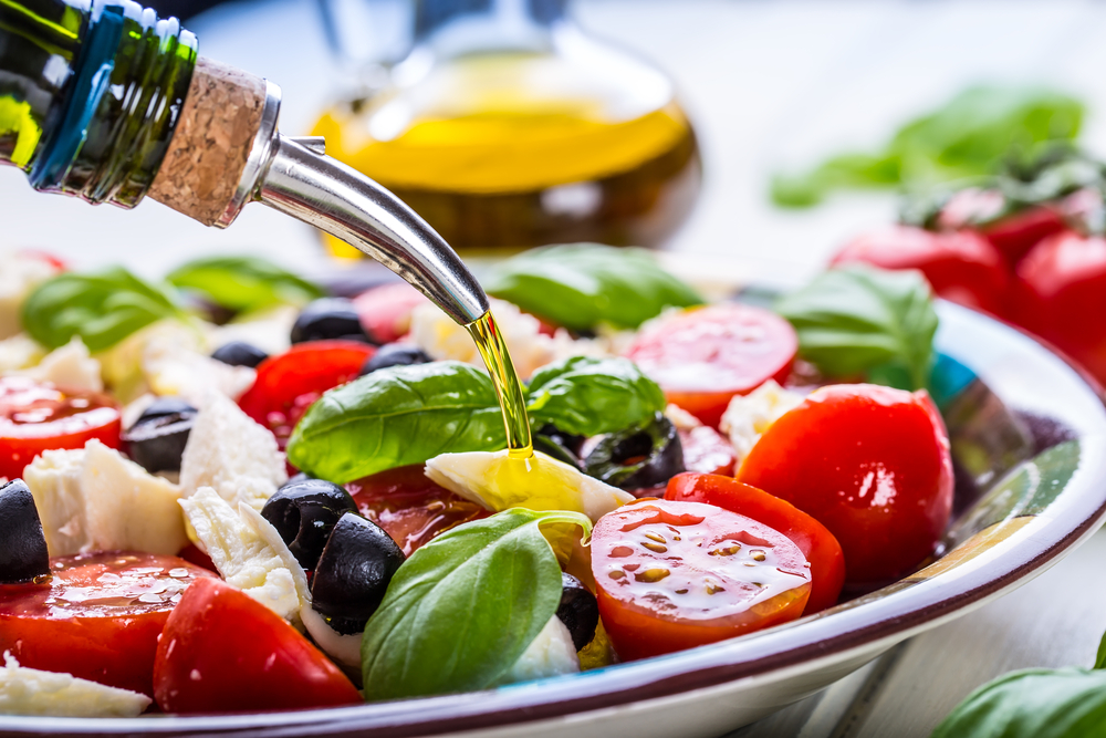 Un bol de salată cu alimente permise în dieta mediteraneană în care se toarnă ulei de măsline
