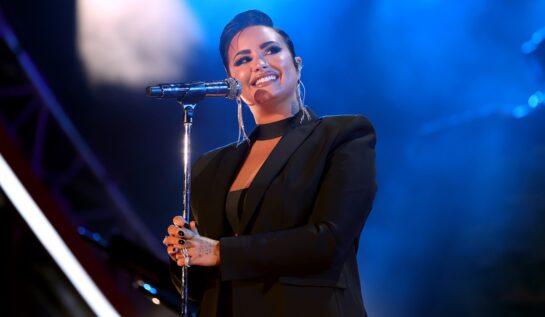 Demi Lovato într-o ținută all black pe scenă în fața unui microfon la concertul susținnut în Los Angeles