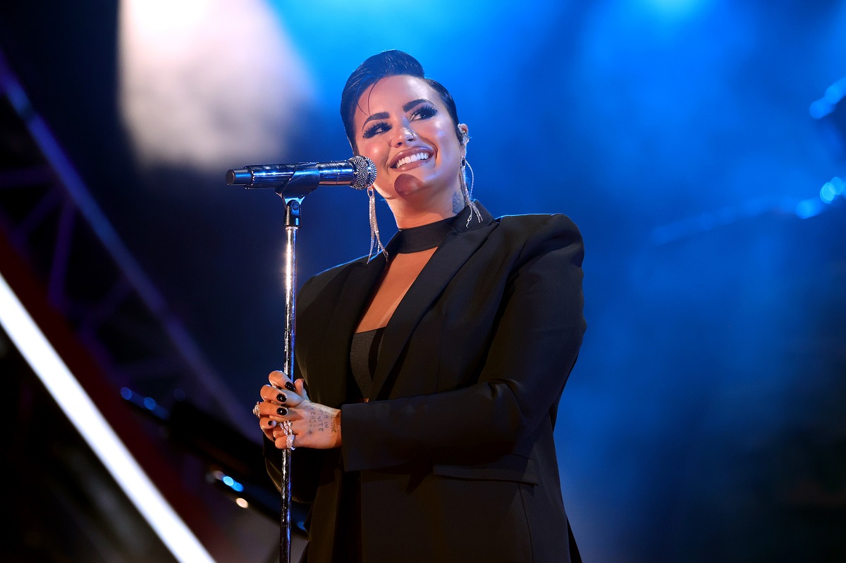 Demi Lovato într-o ținută all black pe scenă în fața unui microfon la concertul susținnut în Los Angeles