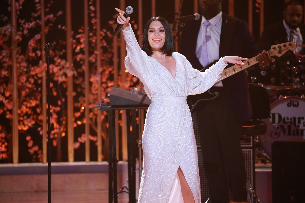 Jessie J într-o rochie albă vaporoasă cu microfonul în mână în timpul unui concert