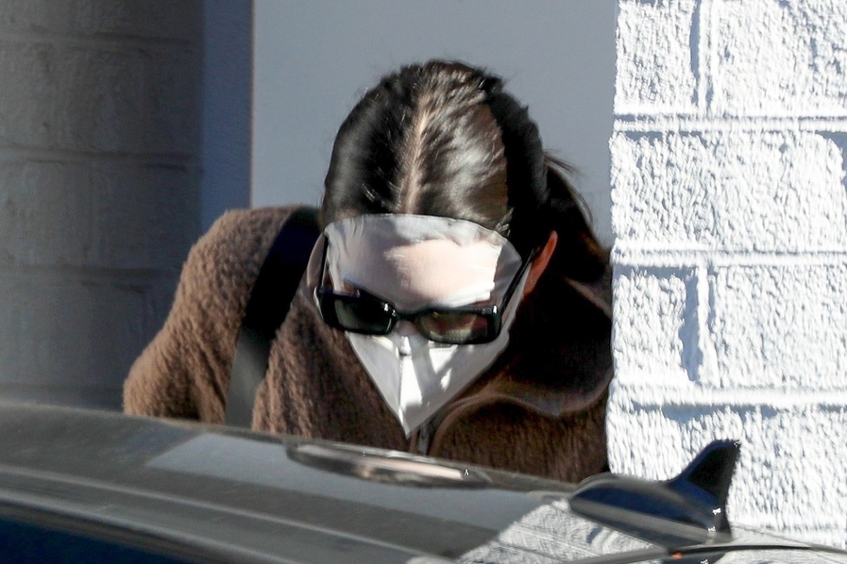 Kendall Jenner cu o mască tip șervețel pe față și o pereche de ochelari de soare în timp ce placă de a un cabinet de înfrumusețare