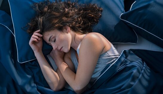 O femeie brunetă care doarme pe o pernă albastră în timp ce este învelită cu o pătură albastră