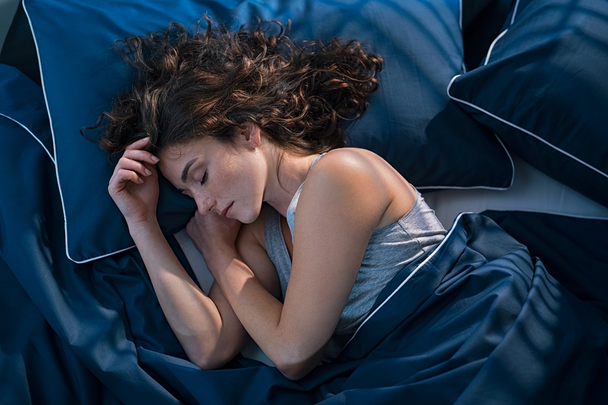 O femeie brunetă care doarme pe o pernă albastră în timp ce este învelită cu o pătură albastră