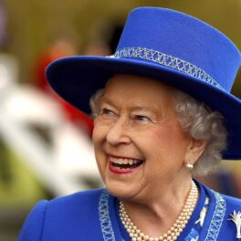 Regina Elisabeta într-un costum albastru în timp ce poartă pălărie și zâmbește la o întâlnire oficială din 2015 din Londra