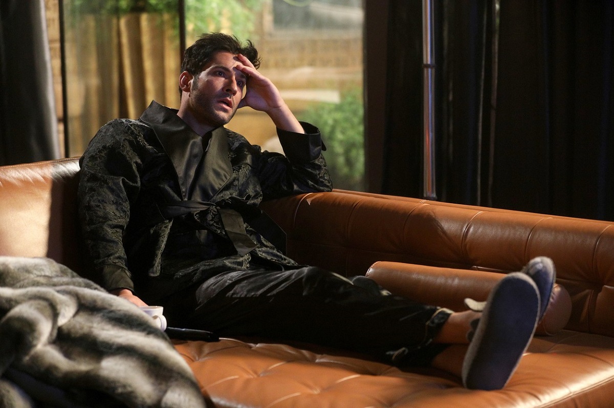 Tom Ellis în pijamale negre în timp ce stă pe o canapea de piele într-una din scenele serialului Lucifer