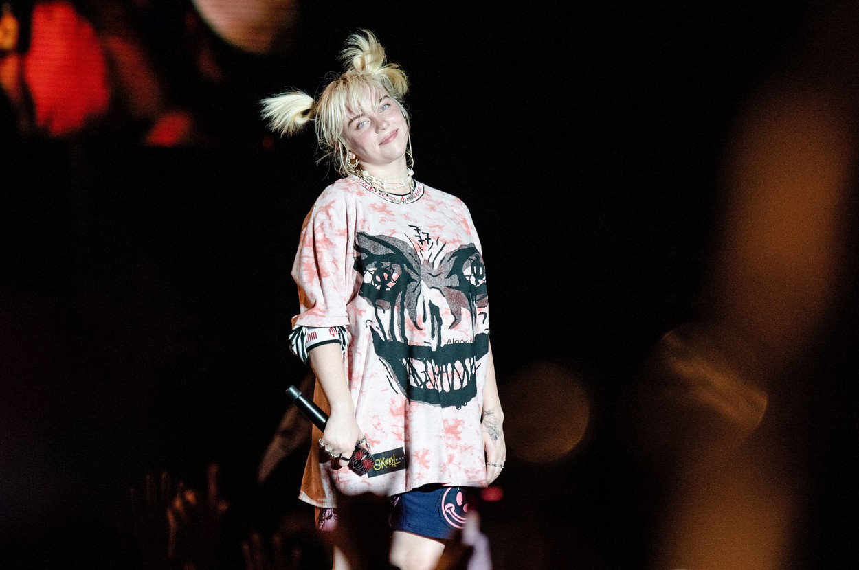 Billie Eilish, la un concert, pe scenă, îmbrăcată în haine largi