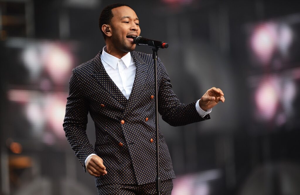 John Legend la costum pe scenă în fața unui microfon în timpul unui concert fiind una dintre cele zece celebrități care și-au schimbat numele