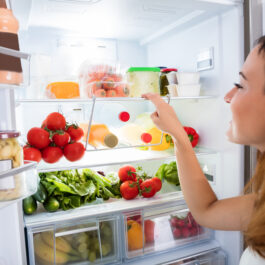 O femeie, în fața unui frigider cu legume și mâncare