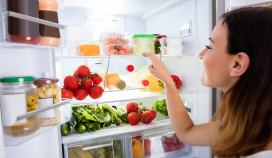 O femeie, în fața unui frigider cu legume și mâncare