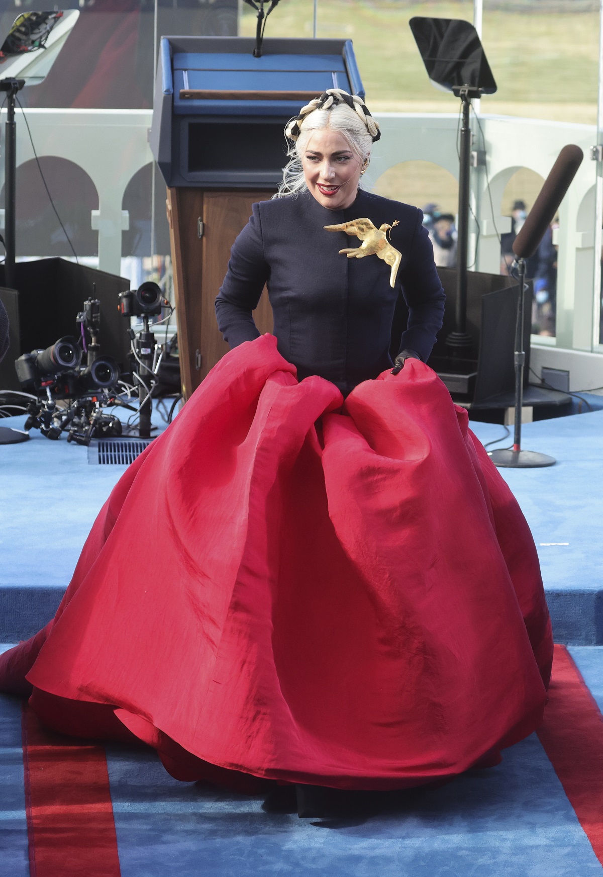 Lady Gaga într-o rochie neagră cu o trenă amplă roșie în timp ce urcă scările de la Capitoliu după ce a cântat imnul național al SUA