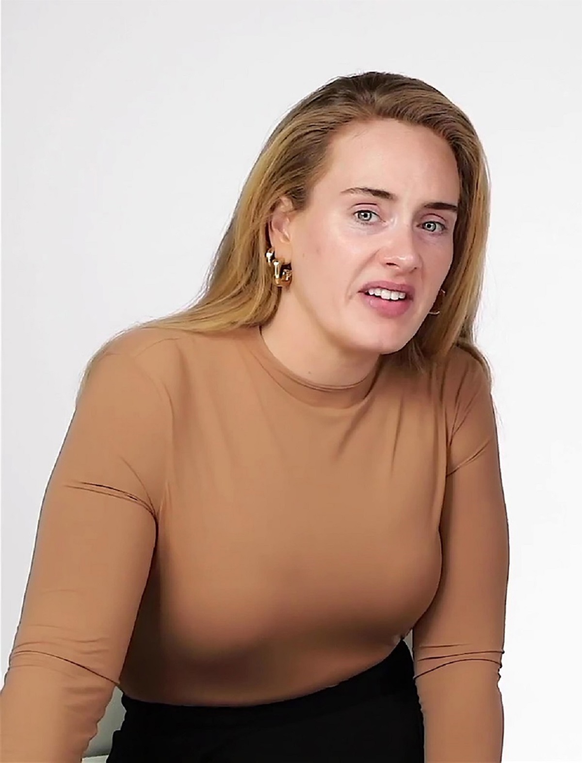 Adele cu părul dat pe spate și o bluză crem în timp ce se pozează nemachiată
