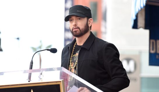 Artistul Eminem cu o șapcă pe cap în fața unui pupitru