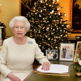 Regina Elisabeta într-o rochie albă în timp ce stă la un birou în fața unui brad de Crăciun