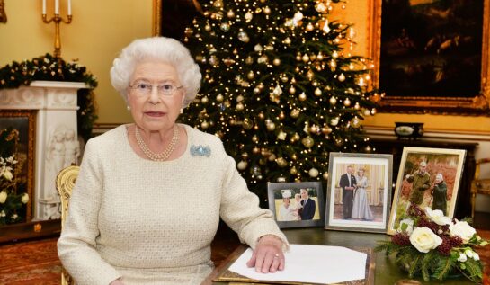Regina Elisabeta într-o rochie albă în timp ce stă la un birou în fața unui brad de Crăciun