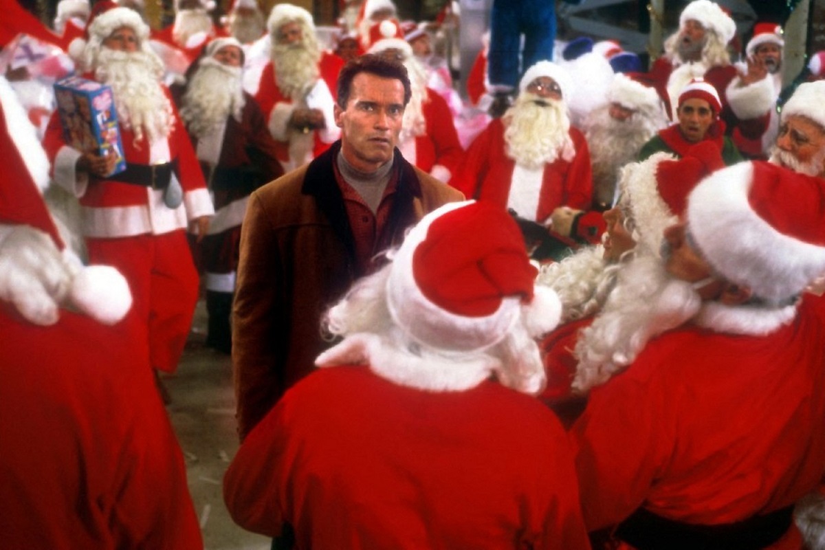 Arnold Schwarzenegger înconjurat de multe persoane îmbrăcate în costum de Moș Crăciun într-unul din cele mai frumoase filme de Crăciun