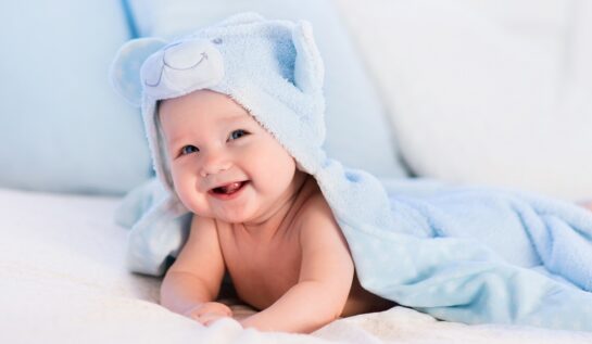 Un bebeluș frumos care stă acoperit de o pătură pufoasă albastră în timp ce zâmbește