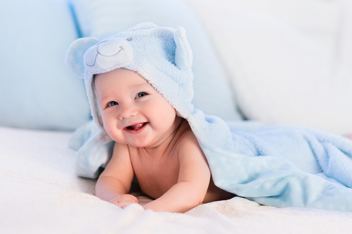 Un bebeluș frumos care stă acoperit de o pătură pufoasă albastră în timp ce zâmbește
